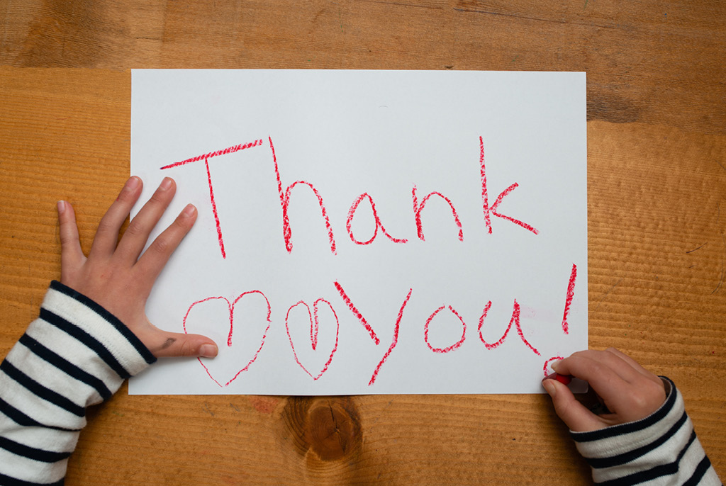 A child making a hand drawn thank you card with a red crayon.
