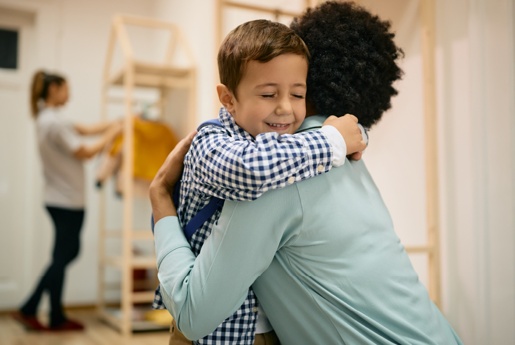 A smiling child hugs their parent goodbye at child care.