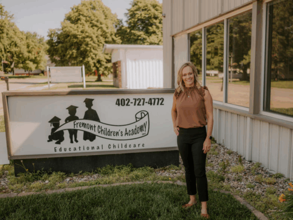 A woman stands smiling in front of a sign that reads