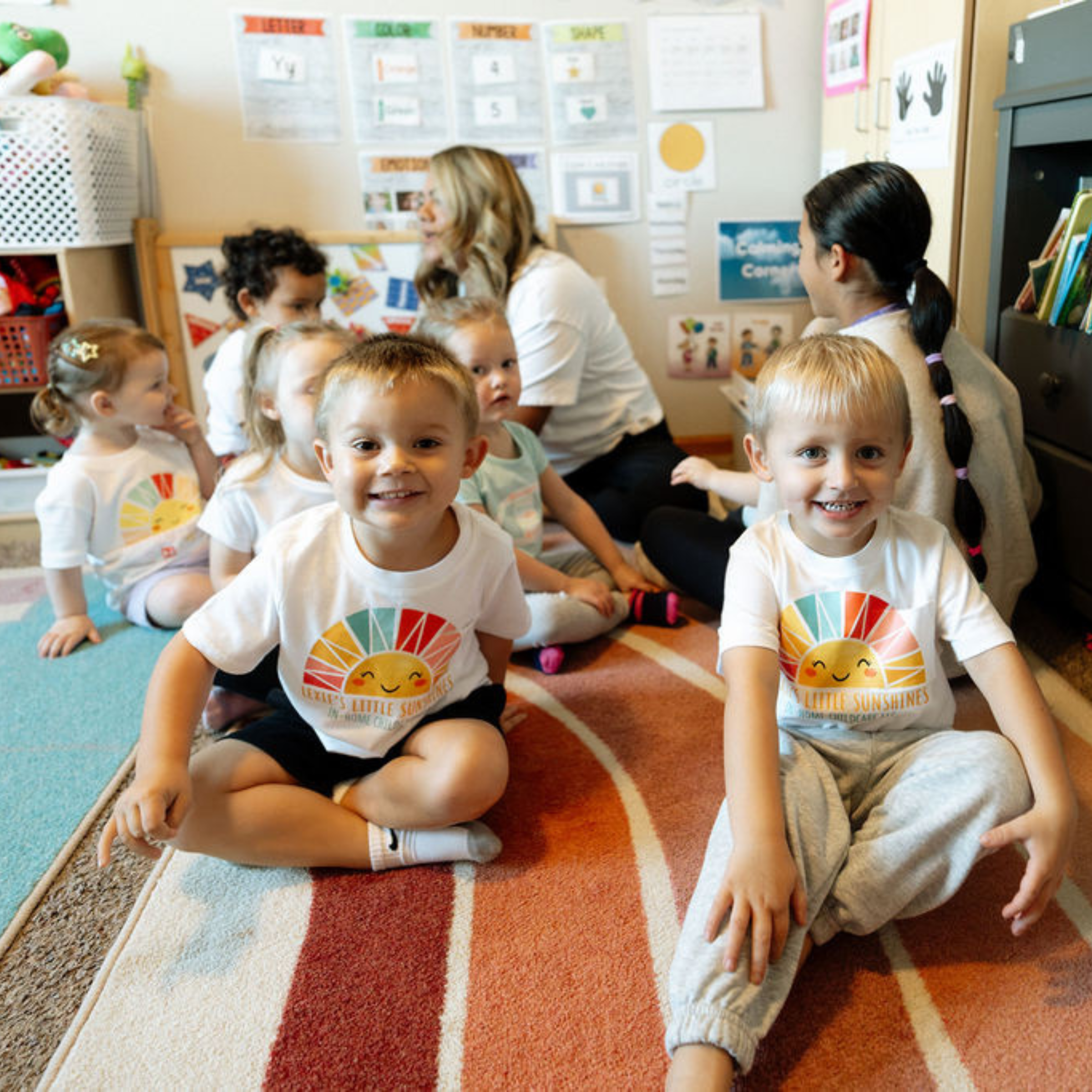 Un grupo de niños pequeños está sentado junto en una alfombra de colores en el aula durante la actividad en grupo.